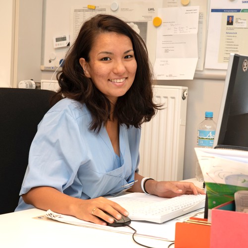 Eine lächelnde Frau mit dunklen, schulterlangen Haaren sitzt an einem Schreibtisch Eine lächelnde Frau mit dunklen, schulterlangen Haaren sitzt an einem Schreibtisch